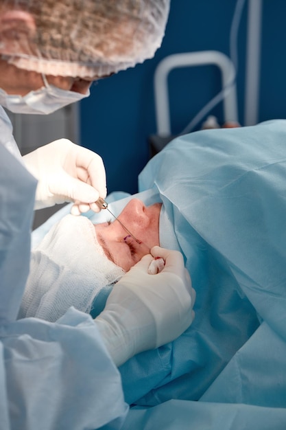 Close-up van het gezicht van een patiënt die ooglidcorrectie ondergaat de chirurg snijdt het ooglid en voert manipulaties uit met behulp van medische instrumenten