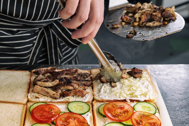 Close-up van het koken van heerlijke sandwiches met gegrild vlees, mayonaise, tomaat, kaas en komkommer