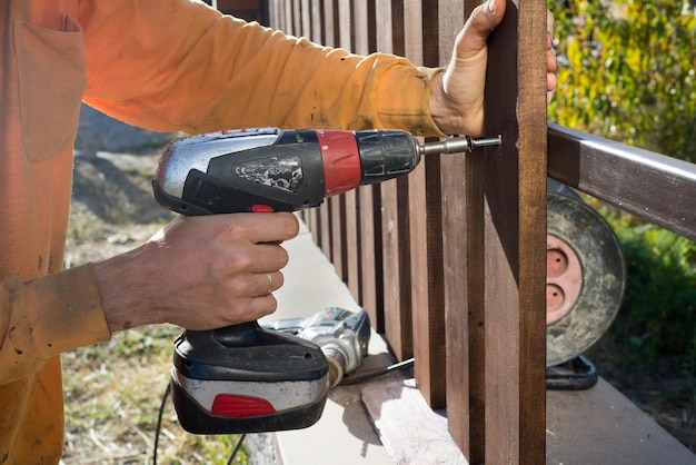 Foto close-up van het met de hand schroeven van een houten plank op een metalen constructie een houten hek bouwen met een boor en een schroef