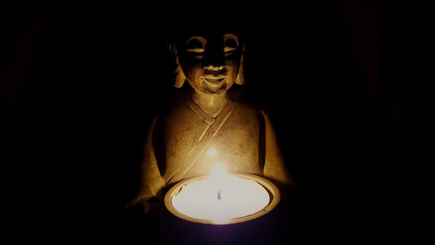 Foto close-up van het standbeeld van boeddha met kaars tegen een zwarte achtergrond