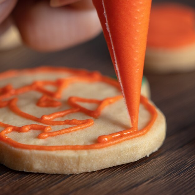 Close-up van het versieren van schattige Halloween pompoen peperkoek koekjes met glazuur