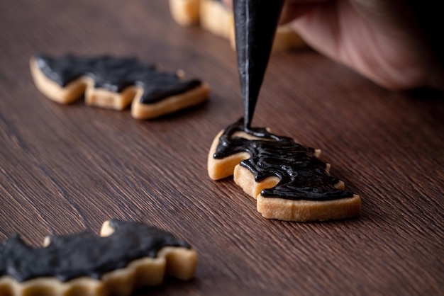 Close-up van het versieren van schattige Halloween vleermuissuikerkoekjes met glazuur
