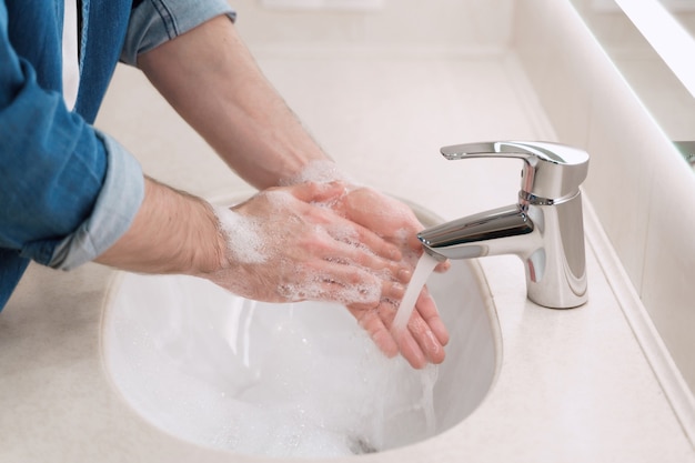 Close-up van het wassen van handen met zeep in gootsteen met stroom heet water om virale en bacteriële infectie te voorkomen. covid-19-preventie