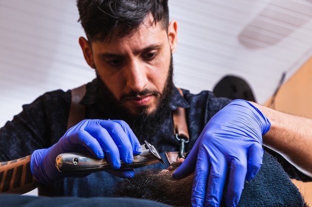 Close-up van het werk van een kapper voor een knappe jongeman met een baard bij de kapper