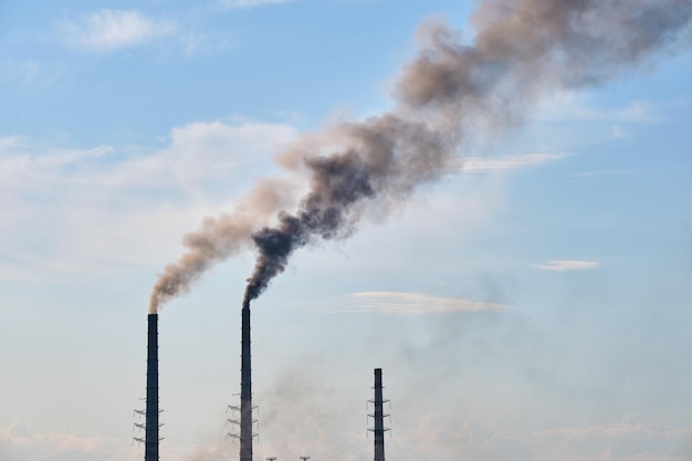 Close-up van hoge pijpen van thermische elektriciteitscentrales met zwarte rook die naar boven vervuilende atmosfeer beweegt. Productie van elektrische energie met fossiele brandstofconcept.