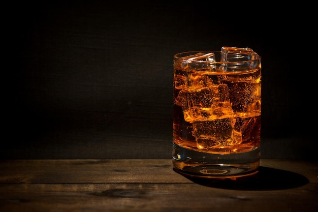 Foto close-up van ijsblokjes in whisky op tafel in de donkere kamer