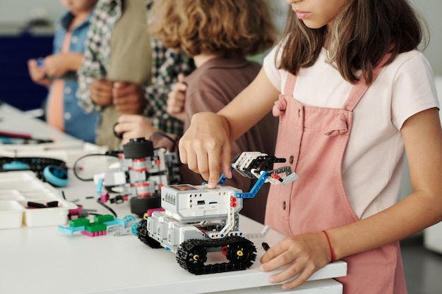 Close-up van jeugdig schoolmeisje dat op de knop bovenop speelgoedrobot drukt