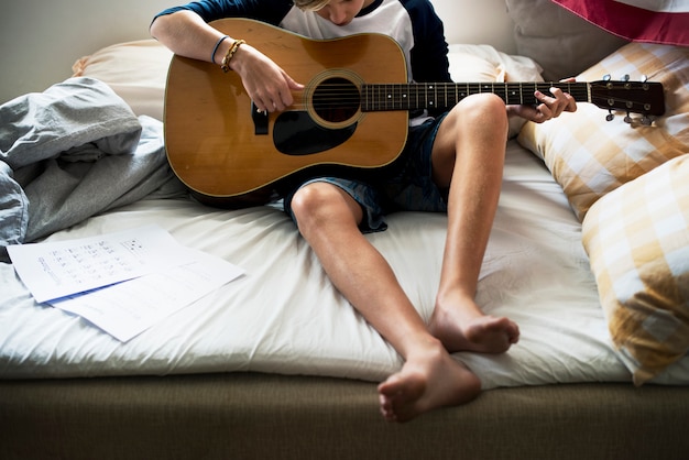 Close-up van jonge Kaukasische jongen gitaarspelen op bed