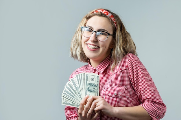 Close-up van jonge mooie vrouw in een rood geruit hemd in glazen met Amerikaans dollarsgeld in hand over grijze achtergrond