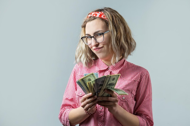 Close-up van jonge mooie vrouw in een rood geruit hemd in glazen met Amerikaans dollarsgeld in hand over grijze achtergrond