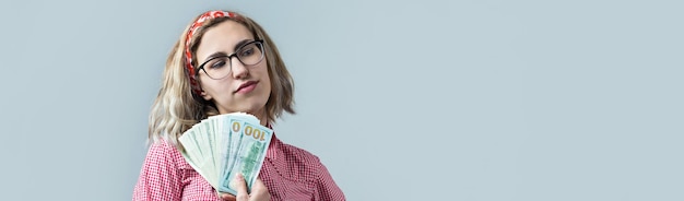 Close-up van jonge mooie vrouw in een rood geruit hemd in glazen met Amerikaans dollarsgeld in hand over grijze achtergrond