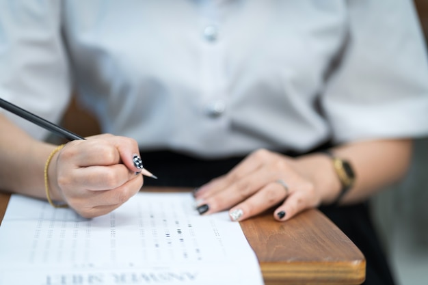 Foto close-up van jonge universiteitsstudenten concentreren zich op het doen van examen in de klas. studente schrijft op het examenpapier in de klas.