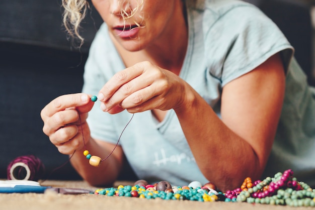 Foto close up van jonge volwassen vrouw bezig met sieraden goedkope houten kralen maken van braelets en ketting. alternatief thuiswerk voor moderne mensen met online winkel