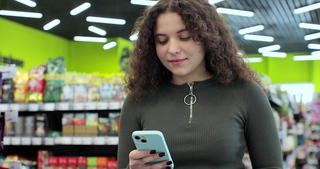 Close-up van jonge vrouw gebruik smartphone in supermarkt Vrouw koper met behulp van mobiele telefoon applicatie staande met winkelwagentje in supermarkt