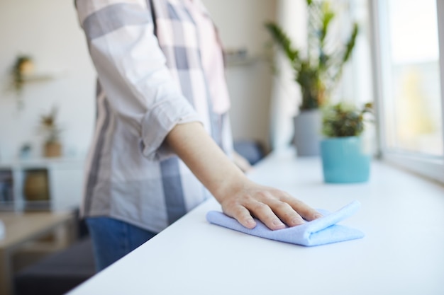 Close-up van jonge vrouw stof met doek afvegen terwijl huishoudelijk werk thuis