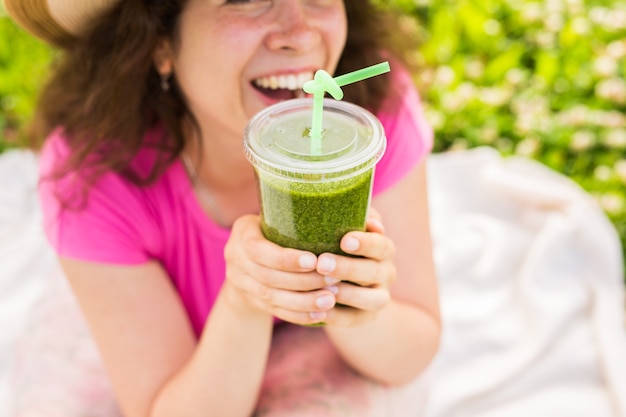 Close up van jonge vrouw veel plezier in het park en groene smoothies drinken tijdens een picknick.