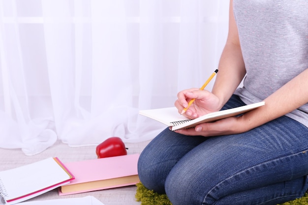 Close-up van jonge vrouwelijke student zittend op de vloer en studeren op lichte achtergrond