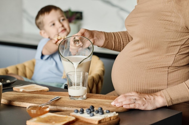 Close-up van jonge zwangere vrouw die verse melk in glas giet voor haar zoon