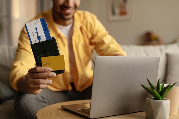 Close-up van jonge zwarte man die laptop gebruikt en hotel online boekt met een creditcard met paspoort