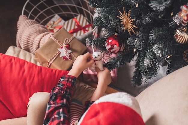Close-up van kindhanden die stuk speelgoed op Kerstboom hangen.