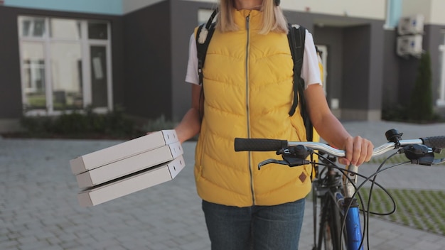 Close up van knappe man open deur naar een pizzabezorger die gele thermische rugzak op een fiets draagt en kartonnen dozen pizza ontvangt Voedselbezorgingsconcept