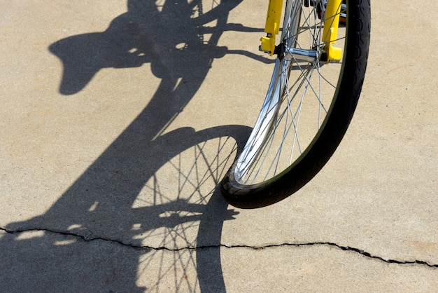 Foto close-up van krom fietswiel, projecterende surrealistische schaduw op stoep