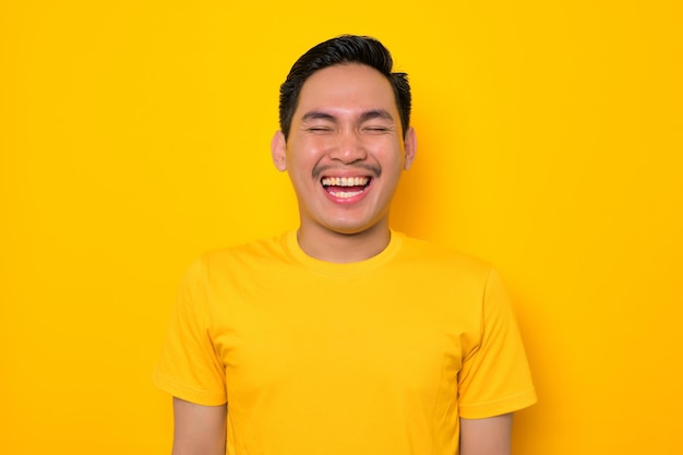 Close-up van lachende jonge Aziatische man in casual tshirt kijken camera geïsoleerd op gele achtergrond Mensen levensstijl concept