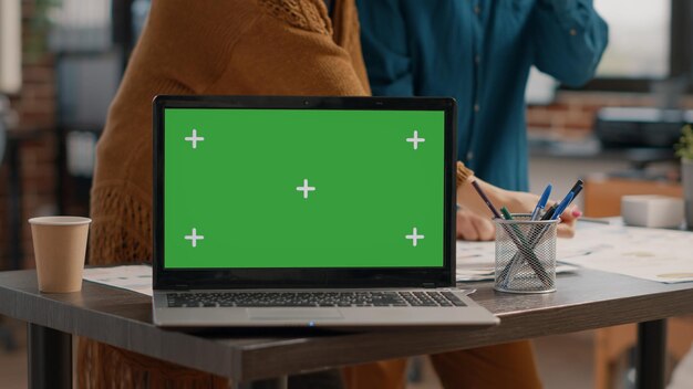 Close up van laptop met horizontaal groen scherm op Bureau bij opstarten kantoor. Computer met geïsoleerde achtergrond en mockup-sjabloon met Chromakey tentoongesteld terwijl mensen aan het werk zijn