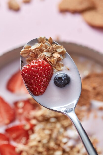 Close-up van lepel met vers, natuurlijk, zelfgemaakt ochtendontbijt met aardbeien, melkdessert, havergranen, bosbessen boven het keramiek van biologisch dessert. Bovenaanzicht.