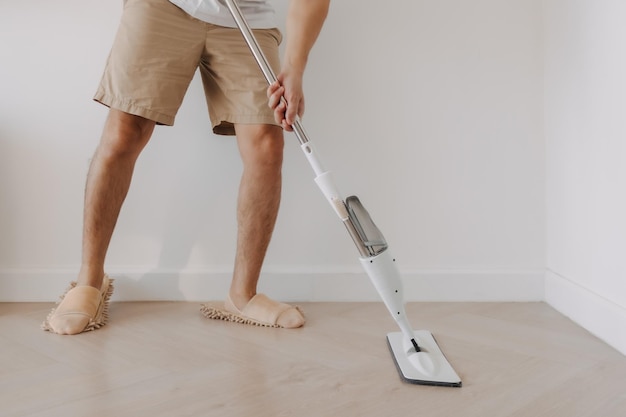 Close-up van man been hand vasthouden en het gebruik van mop voor het schoonmaken van de vloer in de woonkamer appartement man doen