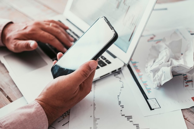 Close up van man handen met mobiele telefoon en laptop computer mensen die werken met grafieken stock market exchange forex concept business zakelijke baan aan de balie online verbinding en communicatie