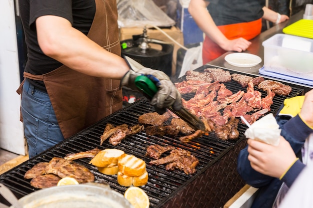 Close up van man met tang vlees grillen op open barbecue op food festival evenement met klanten op zoek op