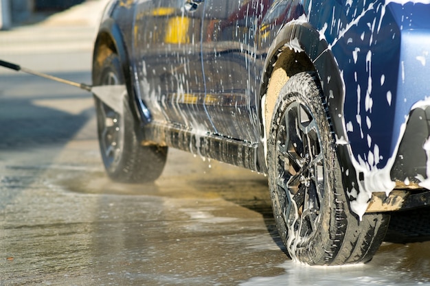 Close-up van mannelijke chauffeur die zijn auto wast met contactloze hogedrukwaterstraal in zelfbedieningsautowasserette.