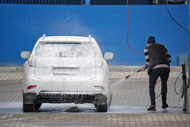 Close-up van mannelijke chauffeur die zijn auto wast met contactloze hogedrukwaterstraal in zelfbedieningswasstraat