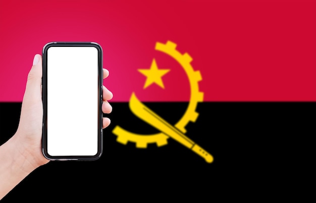 Close-up van mannelijke hand met smartphone met blanco op het scherm op de achtergrond van de vage vlag van angola