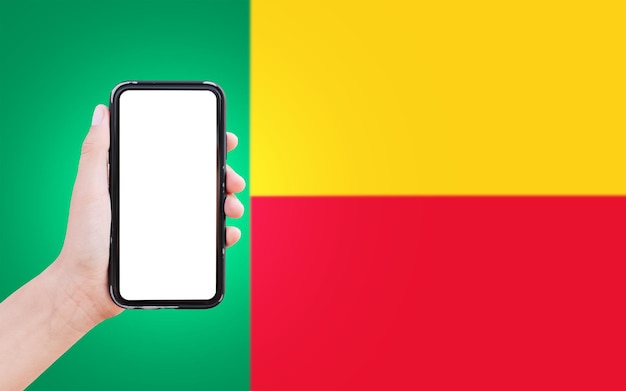 Close-up van mannelijke hand met smartphone met blanco op het scherm op de achtergrond van de wazige vlag van Benin