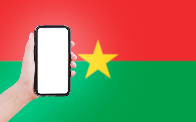 Close-up van mannelijke hand met smartphone met blanco op het scherm op de achtergrond van de wazige vlag van Burkina Faso