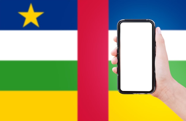 Close-up van mannelijke hand met smartphone met blanco op het scherm op de achtergrond van de wazige vlag van de Centraal-Afrikaanse Republiek