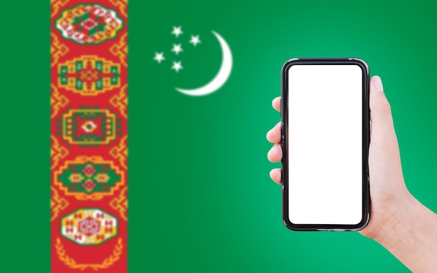 Close-up van mannelijke hand met smartphone met blanco op het scherm op de achtergrond van de wazige vlag van Turkmenistan