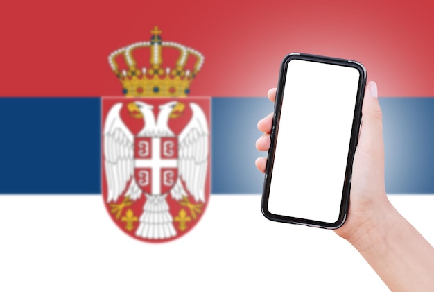 Close-up van mannelijke hand met smartphone met blanco scherm op de achtergrond van wazige vlag van Servië