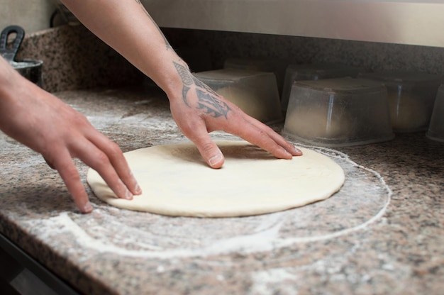 Close-up van mannelijke handen bakker kneedt rauw pizzadeeg Fastfood Pizzabezorging