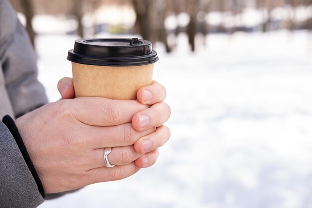 Close-up van mannelijke handen met een papieren beker met koffie op sneeuw achtergrond