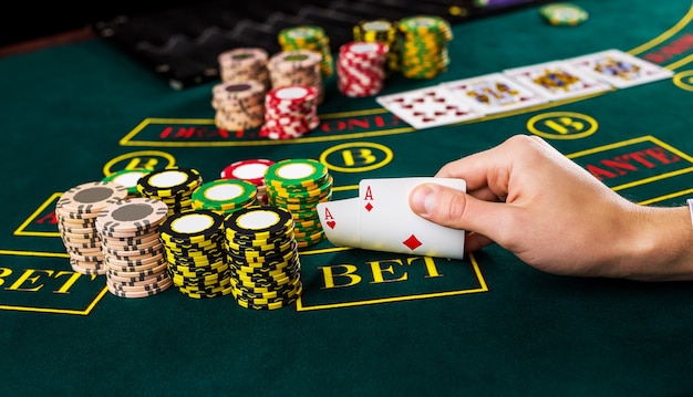 Close-up van mannelijke pokerspeler die de hoeken van twee kaarten azen opheft aan groene casinotafel met azen