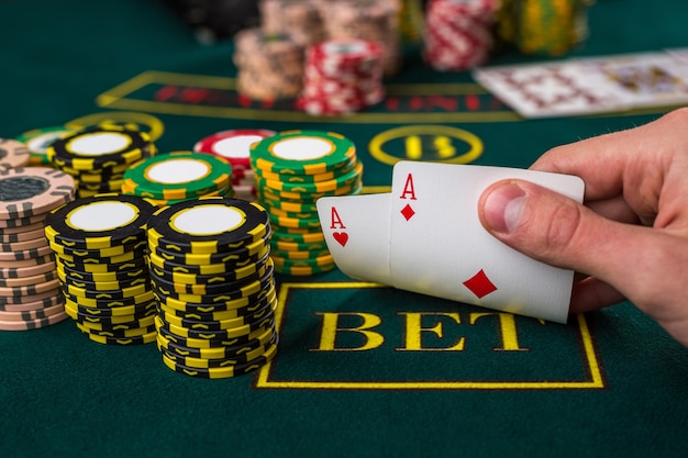 Close-up van mannelijke pokerspeler die de hoeken van twee kaarten azen opheft aan groene casinotafel met azen