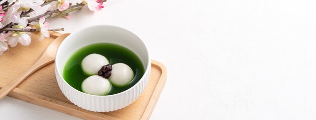 Close up van matcha grote tangyuan (tang yuan) met zoete matcha soep en rode bonenpasta in een kom op witte tafelachtergrond voor festivalvoedsel.