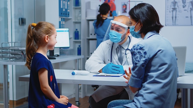 Close up van meisje portret praten met arts over haar symptomen. Kinderarts-specialist in geneeskunde met masker die consultatiebehandeling voor gezondheidszorg in ziekenhuiskast biedt tijdens covid-19