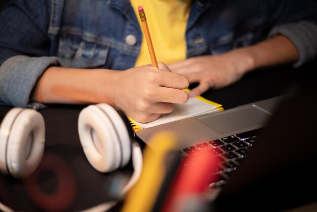 Close-up van meisjes handen maken van aantekeningen met potlood in notebook laptop hoofdtelefoon tienermeisje heeft remot