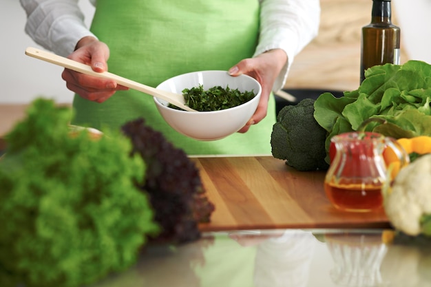 Close-up van menselijke handen die groentensalade in keuken op de glaslijst met bezinning koken. Gezonde maaltijd en vegetarisch concept
