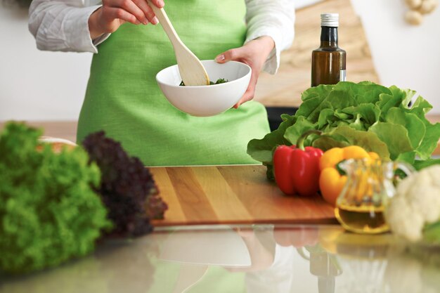 Close-up van menselijke handen die groentensalade in keuken op de glaslijst met bezinning koken. Gezonde maaltijd en vegetarisch concept