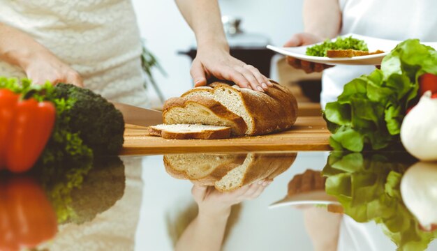 Foto close-up van menselijke handen die in keuken koken moeder en dochter of twee vrouwelijke vrienden die brood snijden voor diner vriendschapsfamilie en levensstijlconcepten